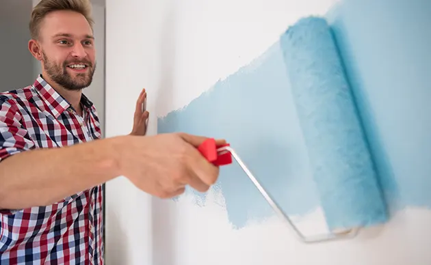 Painter rolling fresh white paint onto an interior wall near a window
