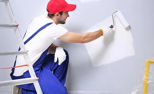 Worker using an angled brush to cut in paint along ceiling trim