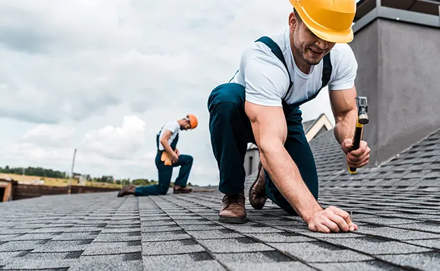 Roofing contractor nailing asphalt shingles on a pitched residential roof