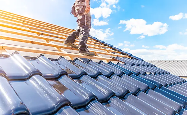 Two roofers installing underlayment and shingles on a house roof in daylight