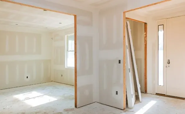 Worker sanding patched drywall joints on an interior wall before painting